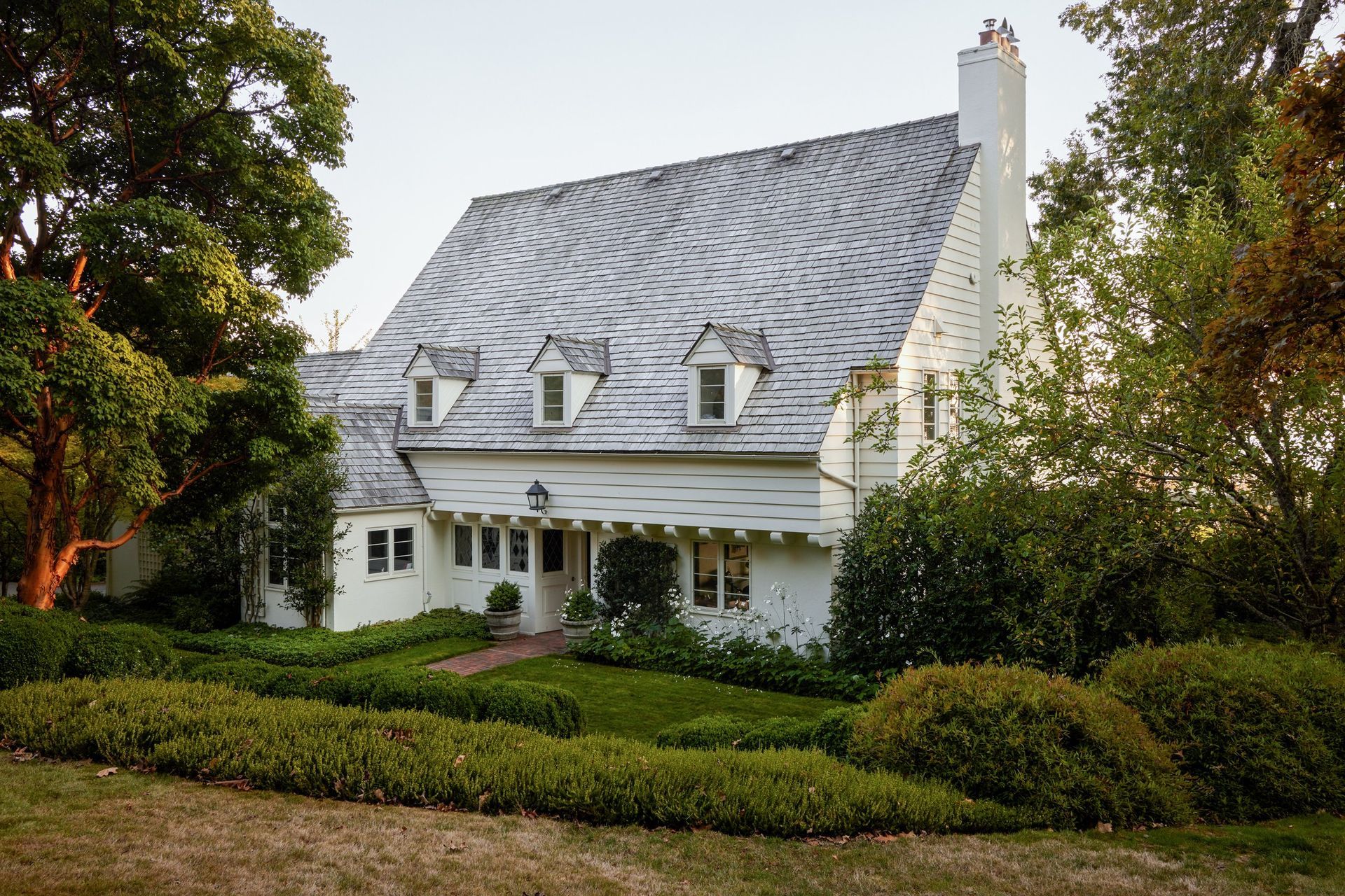a large white house with a slate roof is surrounded by trees and bushes