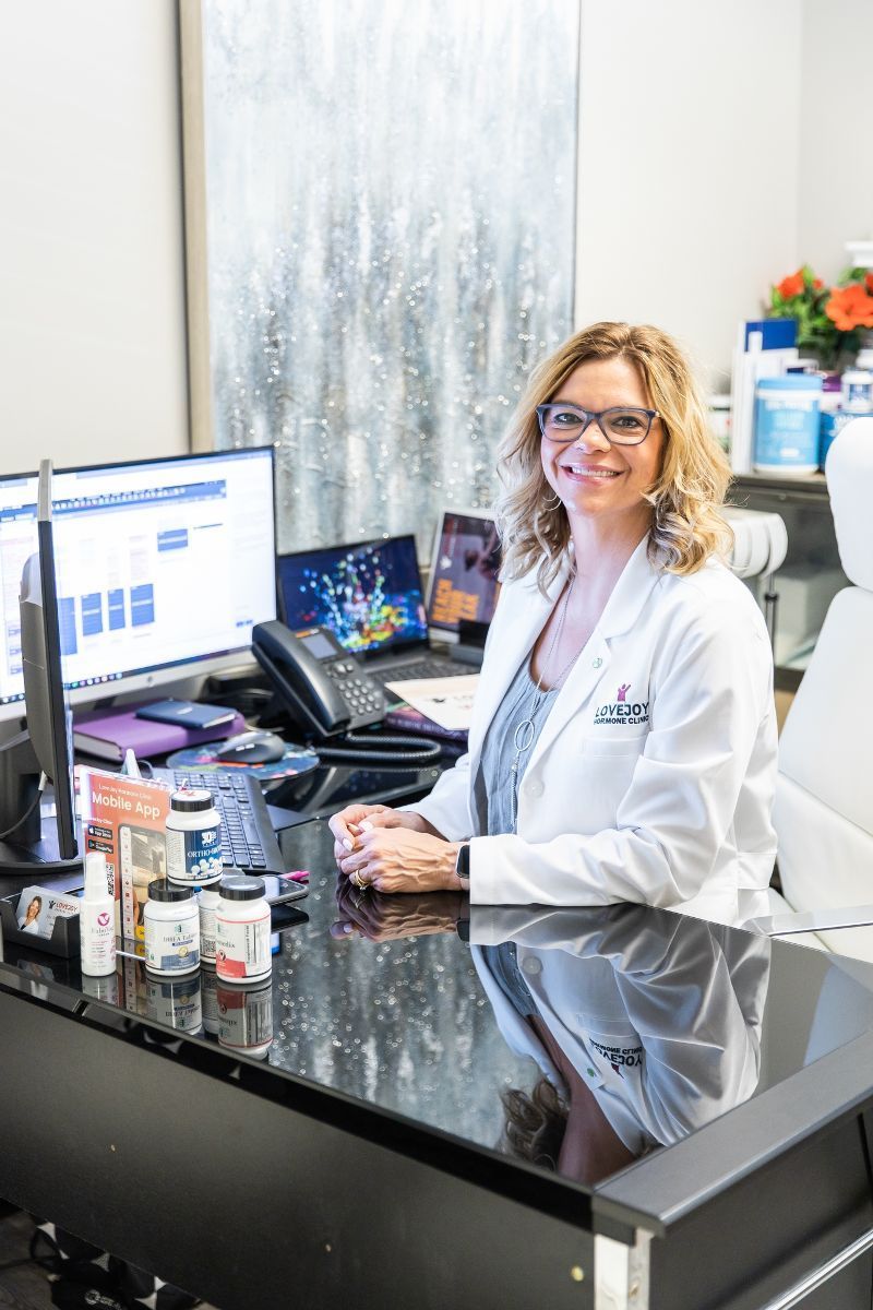 A woman in a lab coat is sitting at a desk in front of a computer.