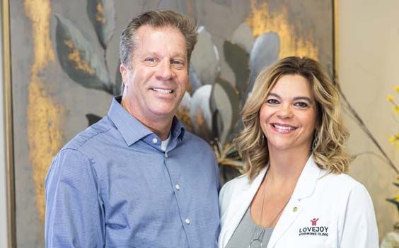 Jon and Joy Melby posing for a picture in front of a painting.