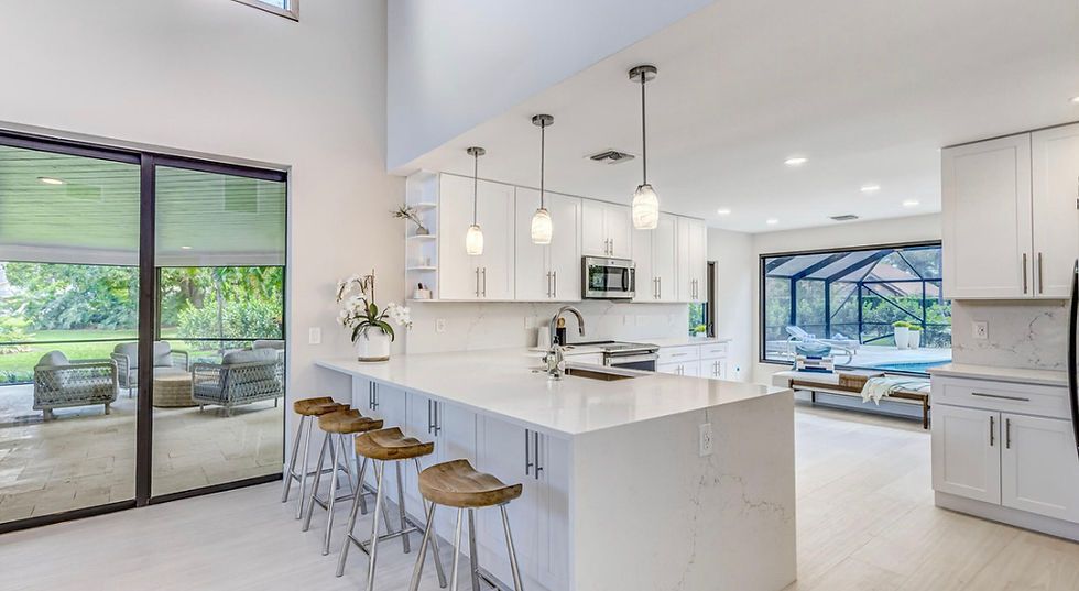A kitchen with white cabinets , a large island , and stools.