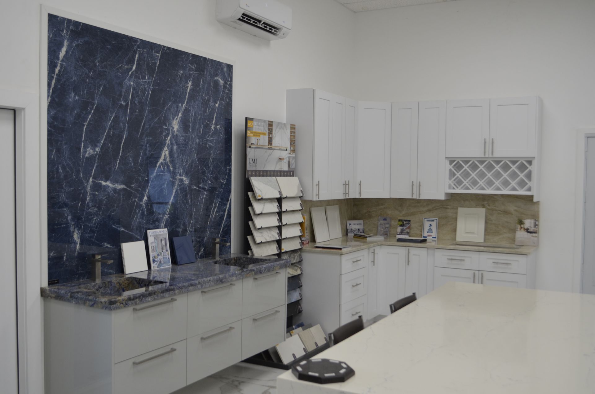 Kitchen showroom with white cabinets, granite countertops, and marble accent wall.