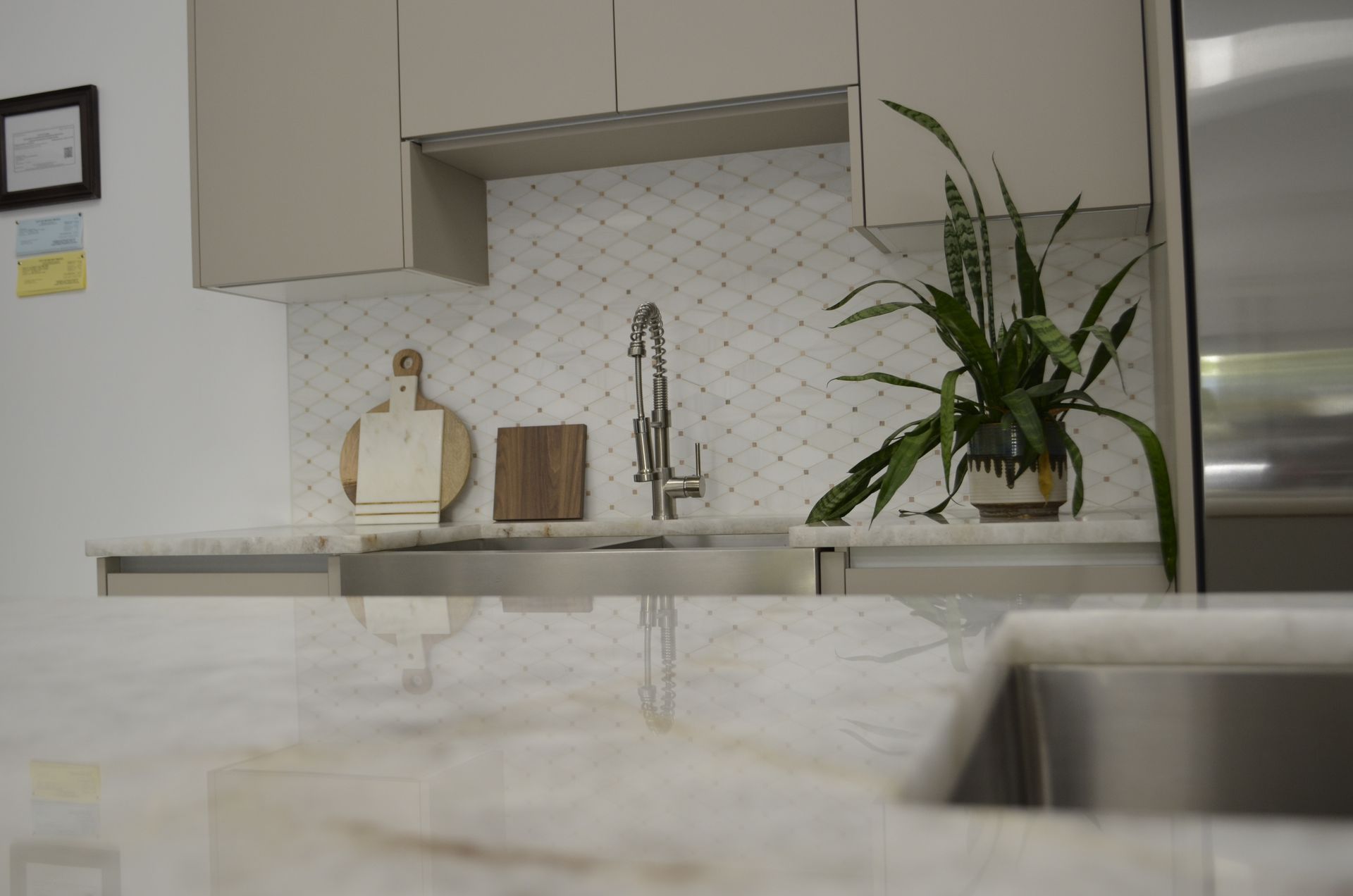 Kitchen with light cabinets, patterned backsplash, sink, and countertop with a plant.