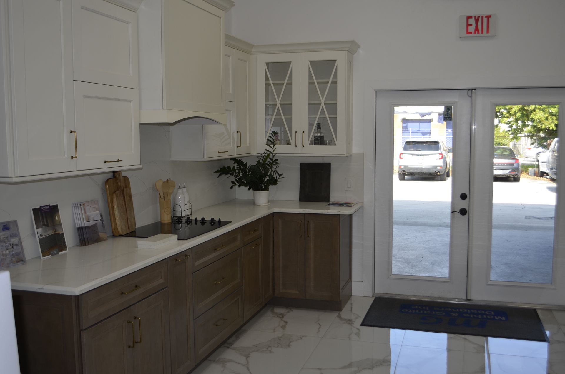 Kitchen display with two-tone cabinets: white uppers, brown lowers. Glass doors lead outside.