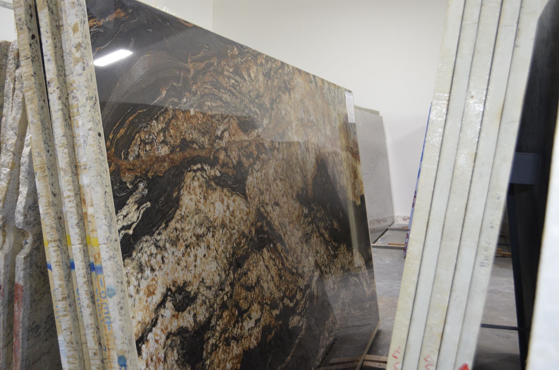 Large slabs of granite, featuring brown, black, and gold veining, are stacked vertically in a warehouse.