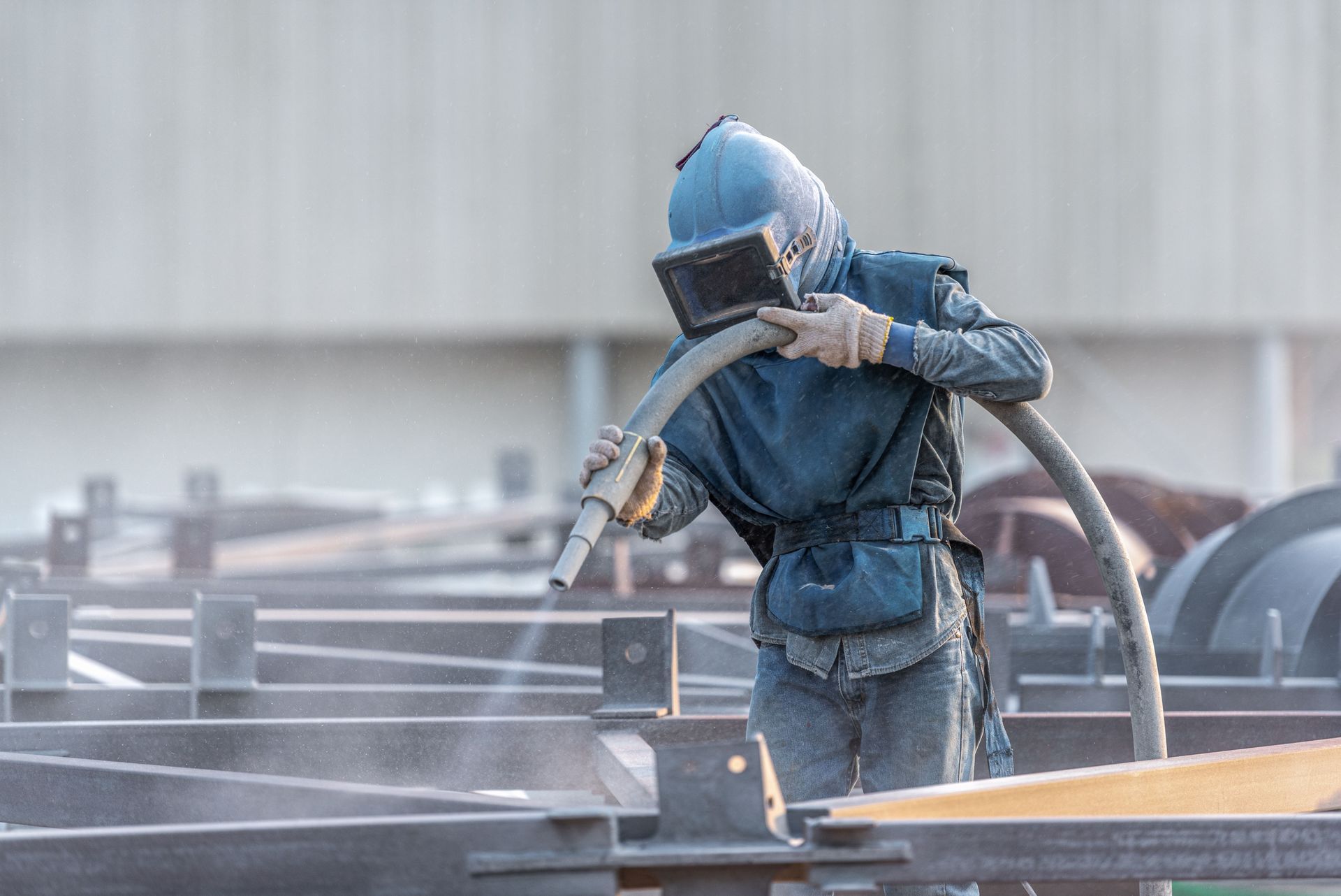Person sandblasting metal structures while wearing protective gear.