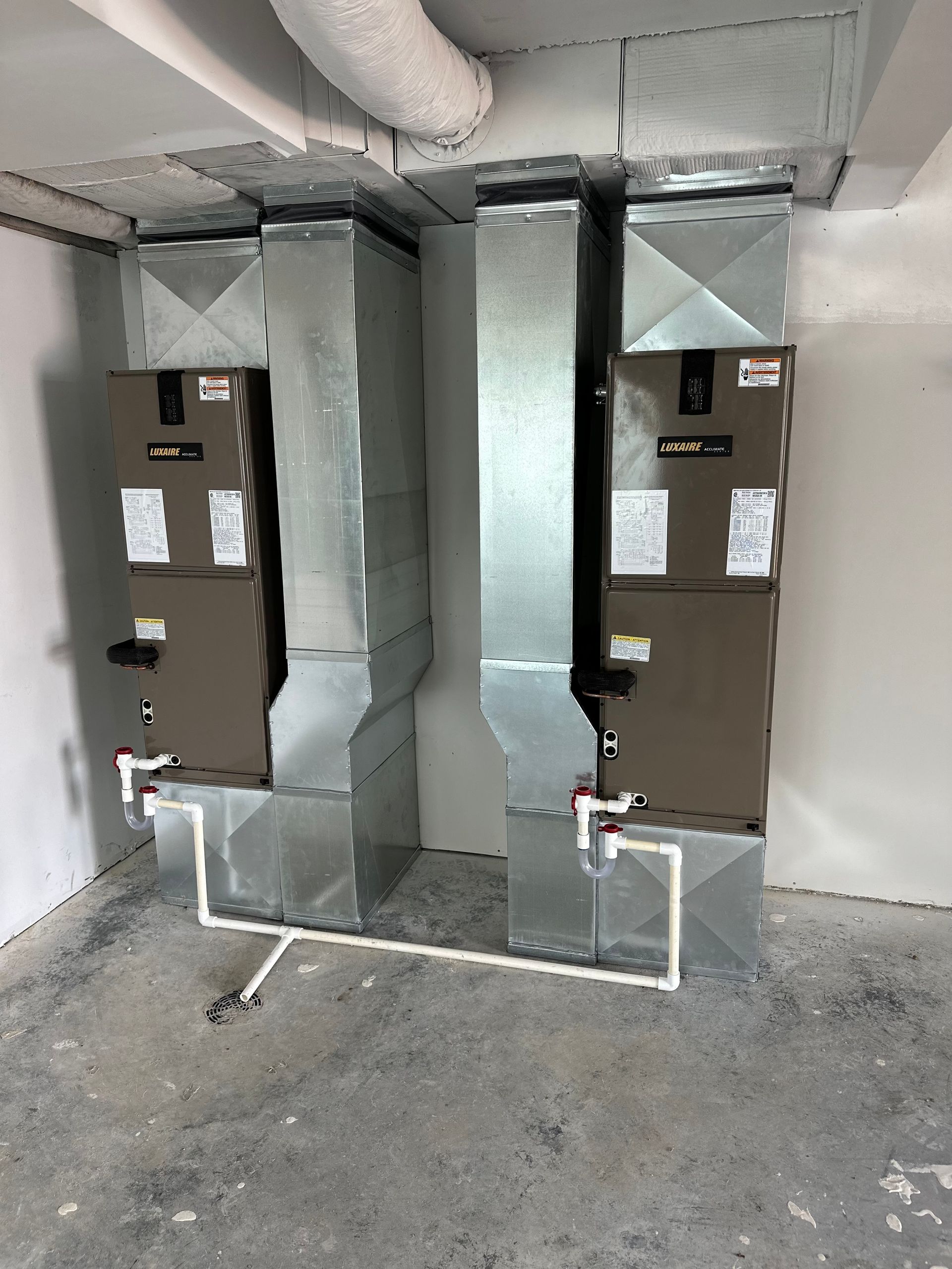 Two HVAC units with ductwork in a room with a concrete floor and white walls.