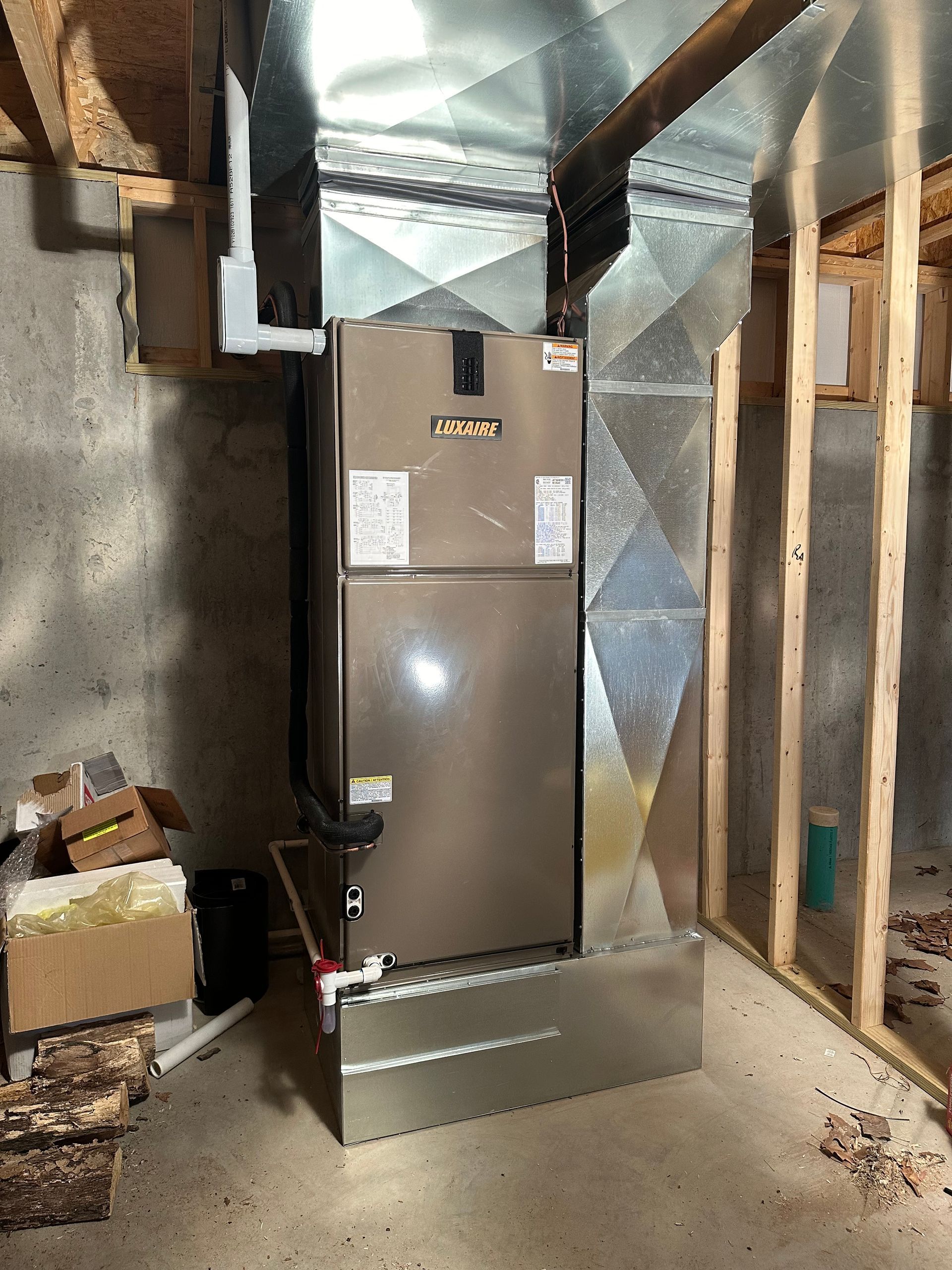 Furnace unit in a basement, with ductwork and framing visible.