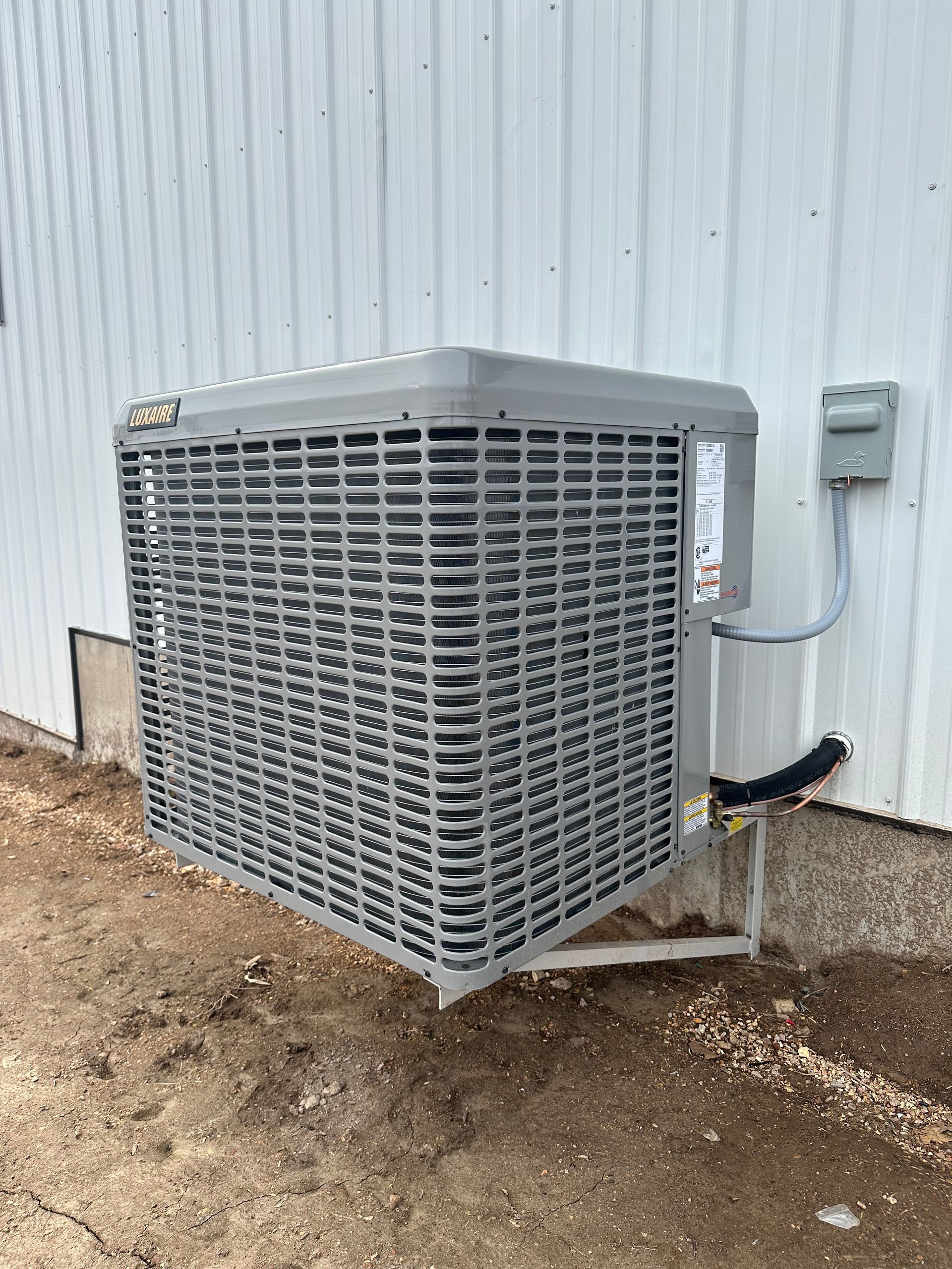 Air conditioner unit on a gray metal bracket outside a building with white siding.