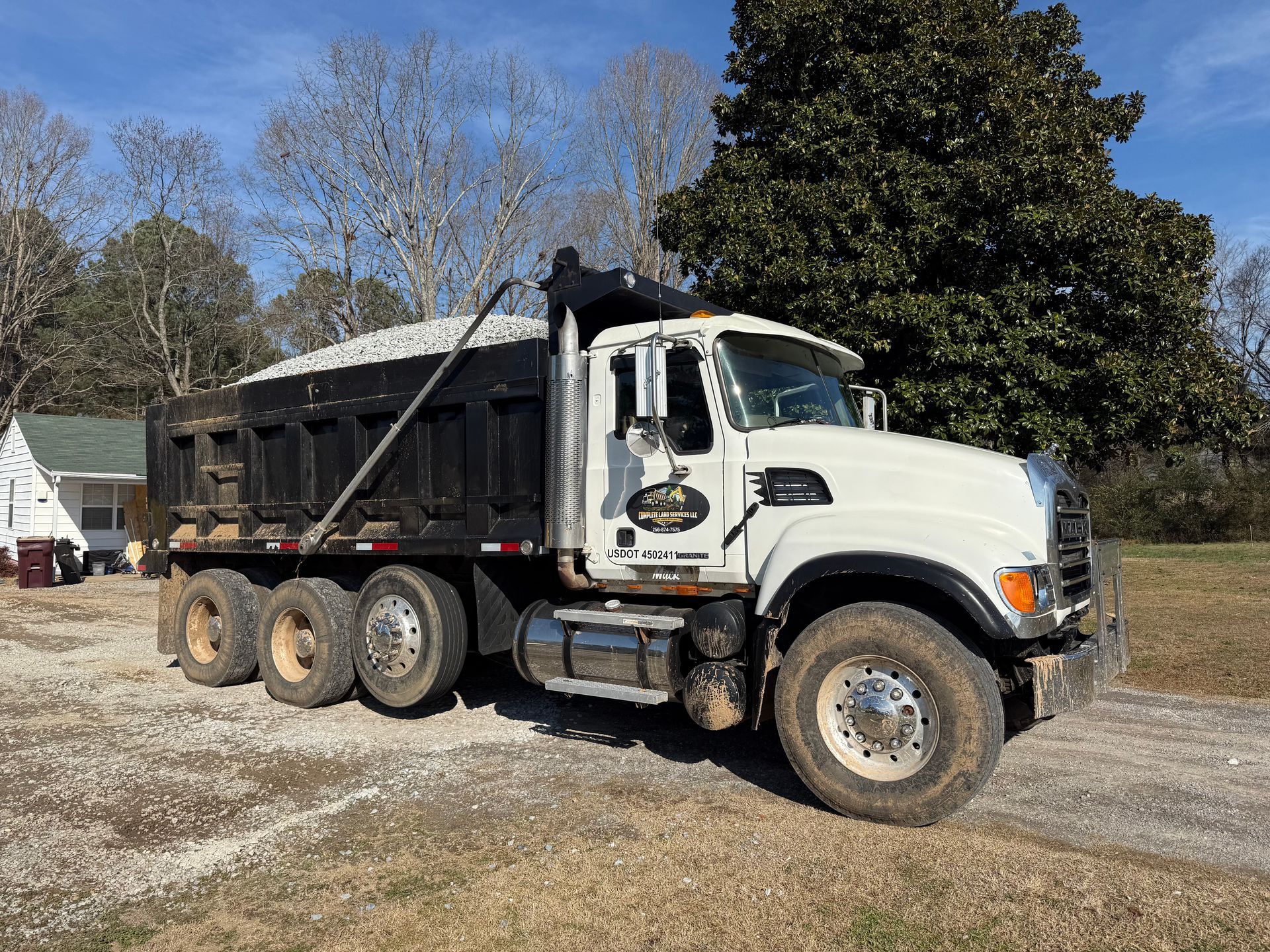 White dump truck loaded with gravel parked on a gravel driveway.