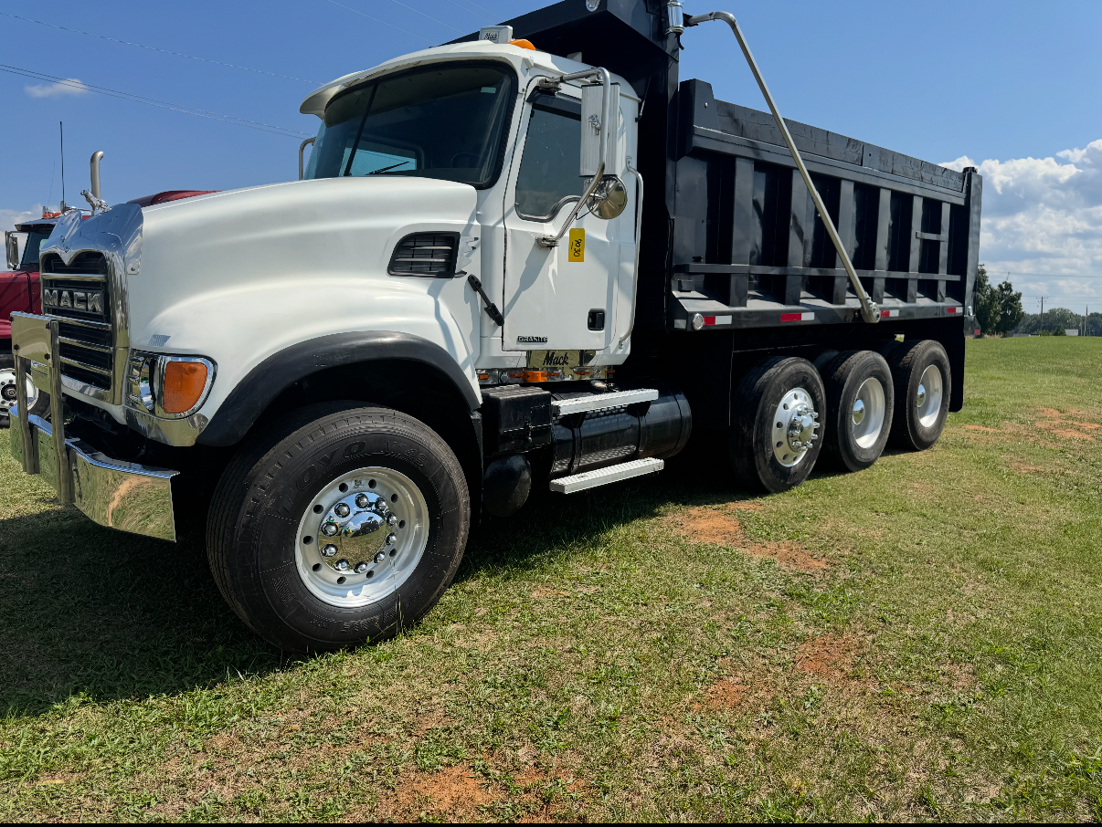 White Mack dump truck parked on a grassy field on a sunny day.