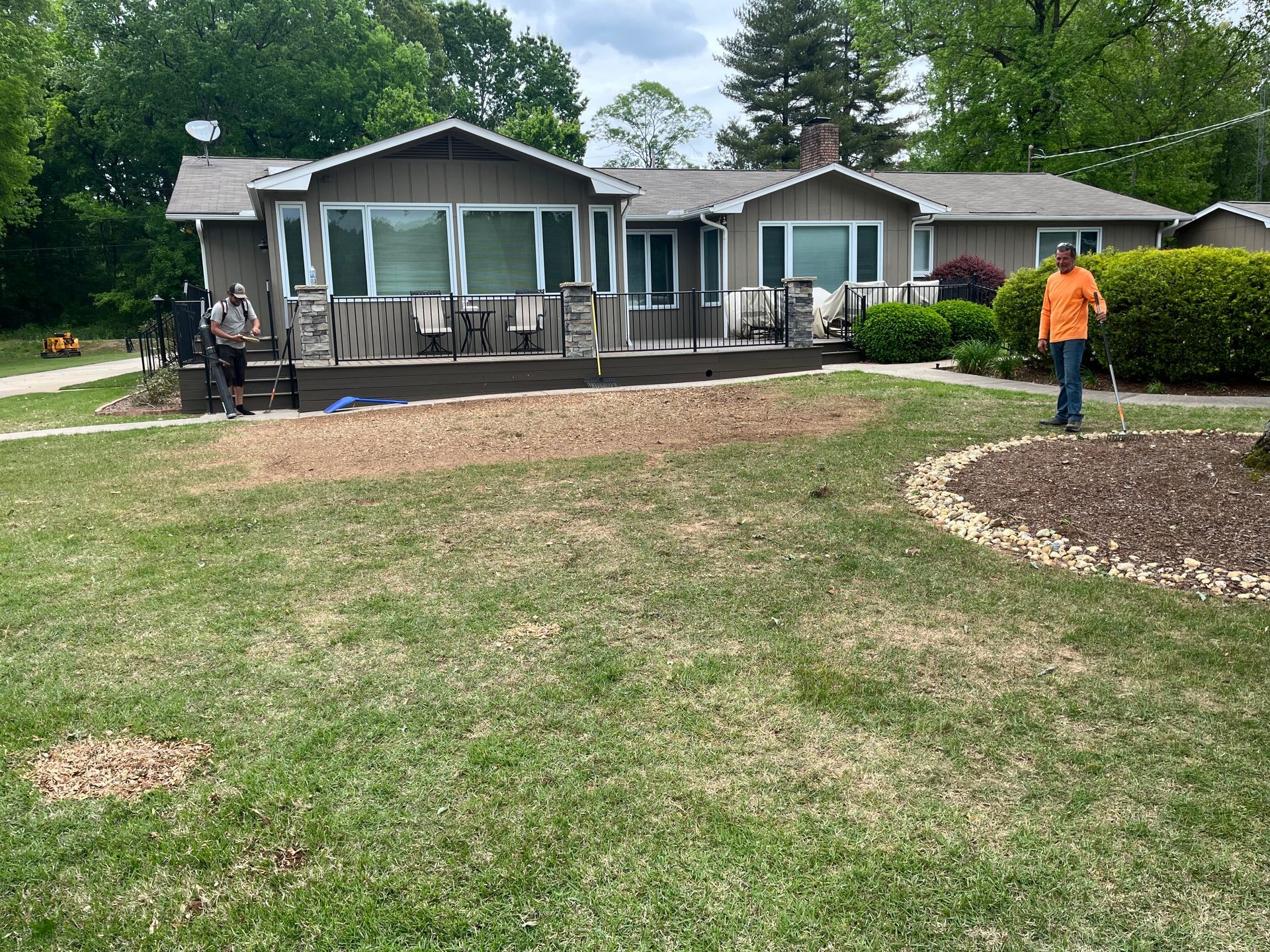 A man in an orange shirt is standing in front of a house.