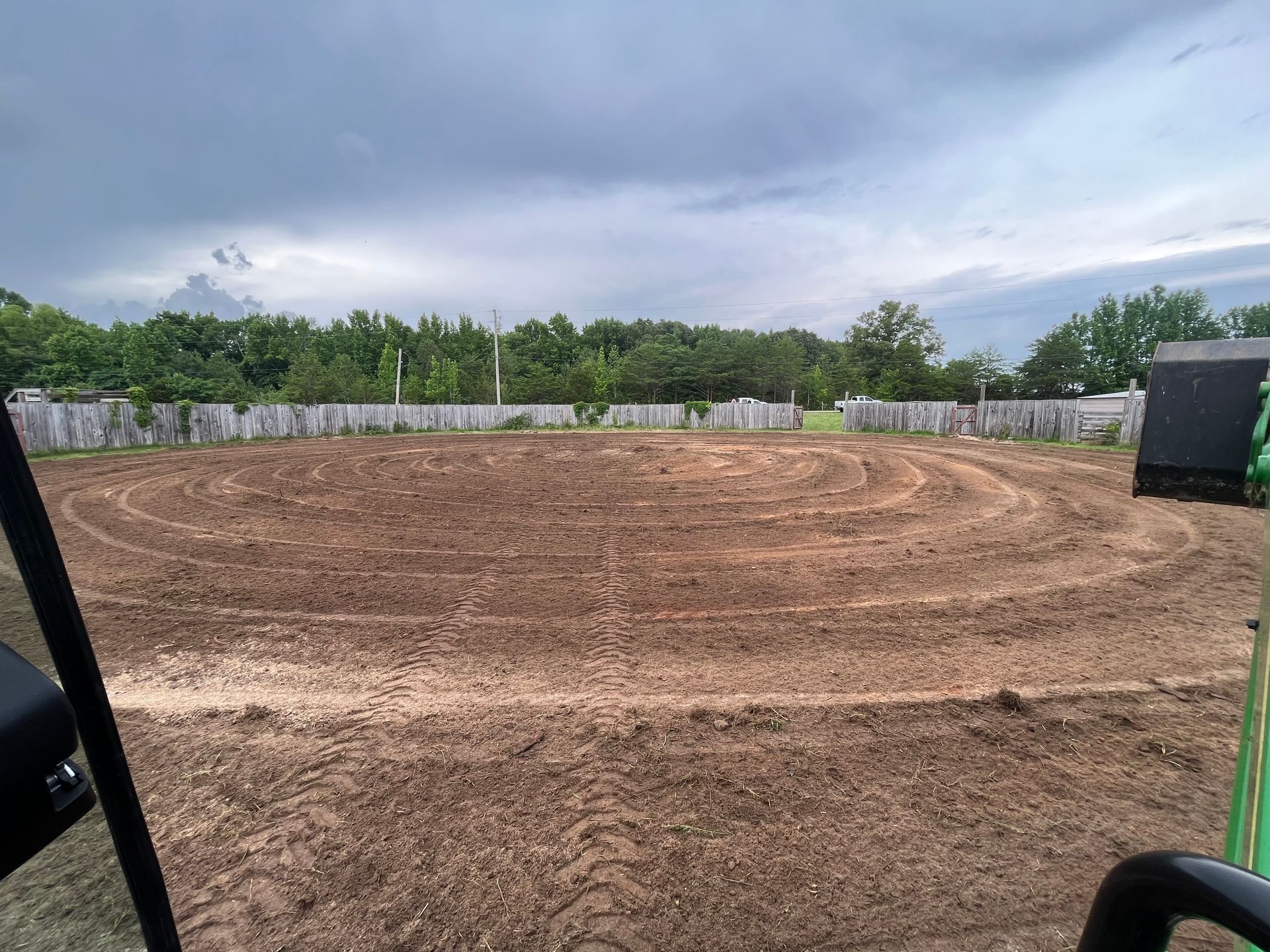A tractor is driving through a dirt field with trees in the background.