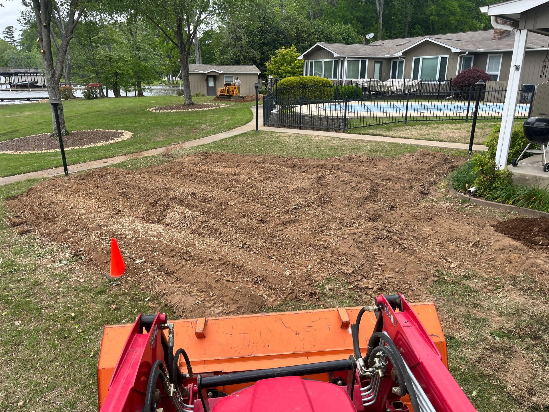 A red tractor is sitting on top of a dirt field in front of a house.
