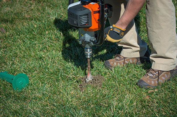 Person using a power auger to drill a hole in grassy ground.