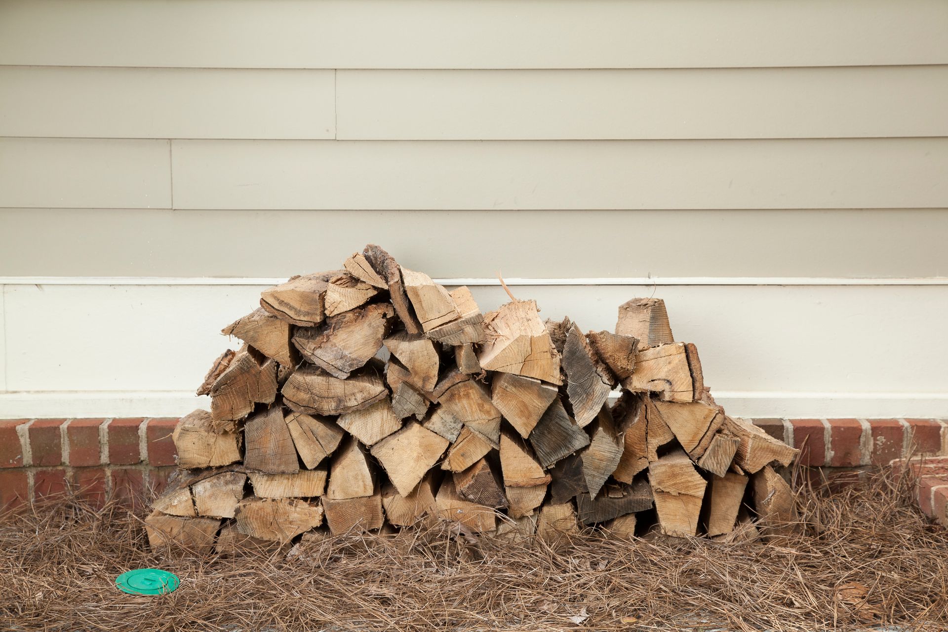 Pile of firewood stacked against a beige wall and red brick base.
