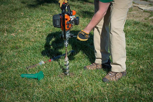 Person using a gas-powered auger to drill into the grass in a yard.