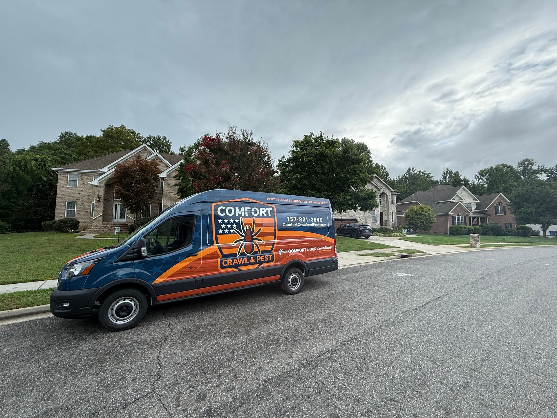 Blue and orange Comfort Experts van parked on a residential street. Houses with trees in the background under a cloudy sky.
