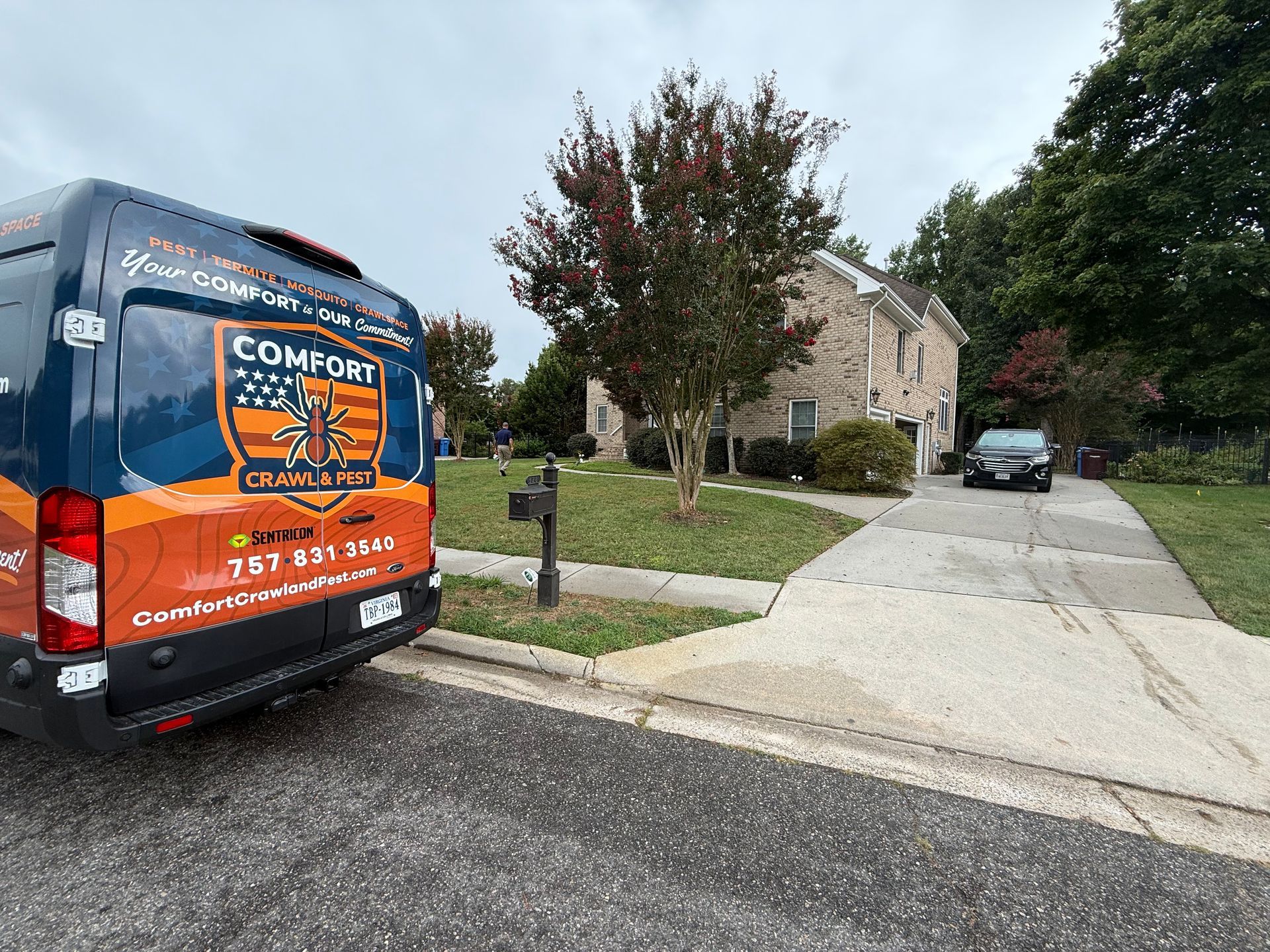 Blue and orange Comfort Experts van parked in front of a house, driveway visible, cloudy sky.