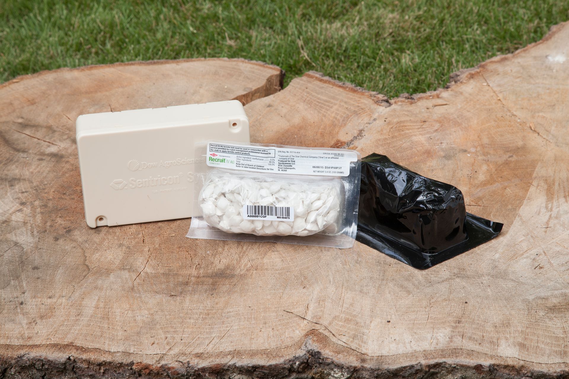 Beige box, packaged white material, and black plastic container on a wooden surface, grass in the background.
