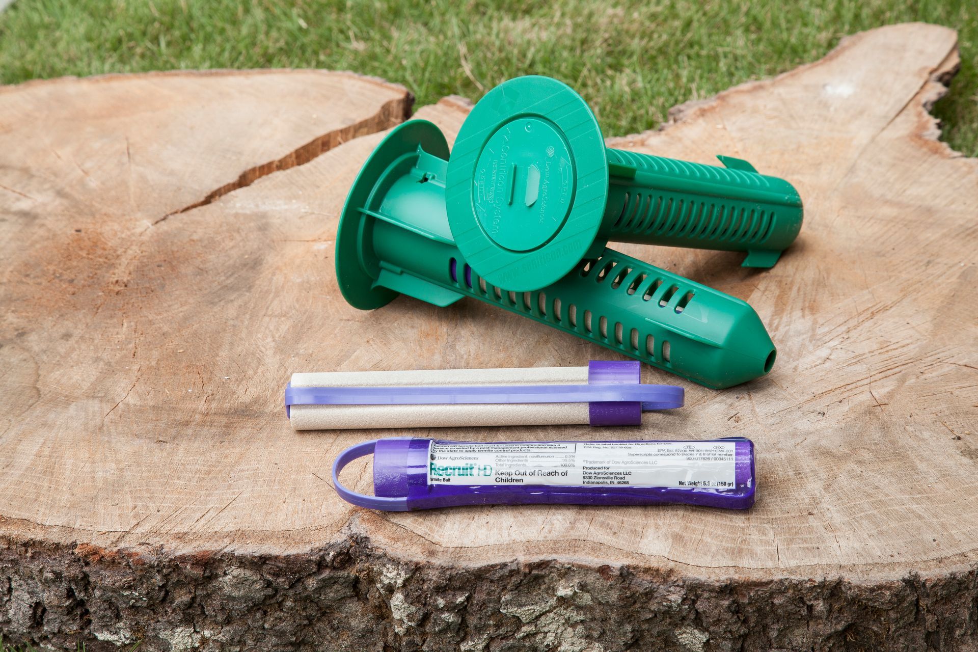 Green termite bait stations and two purple bait cartridges on a tree stump.