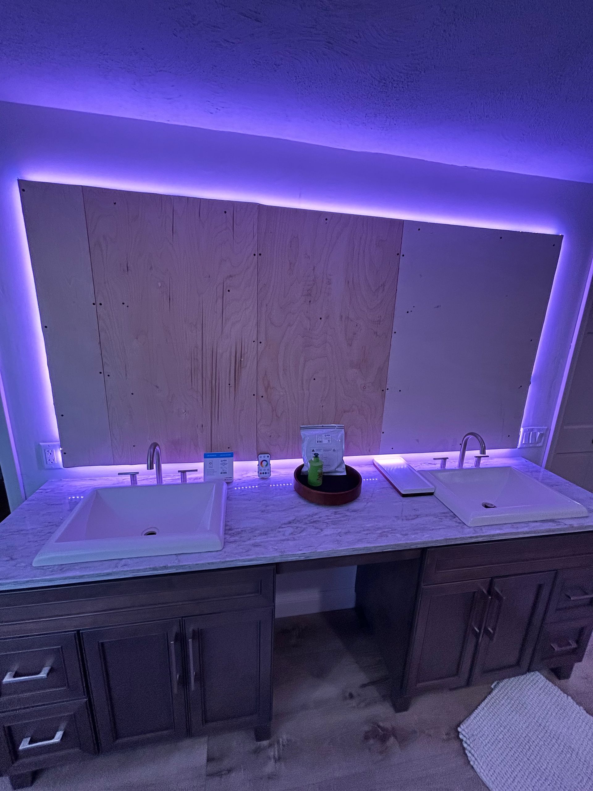 A bathroom with two sinks , a mirror and purple lights.