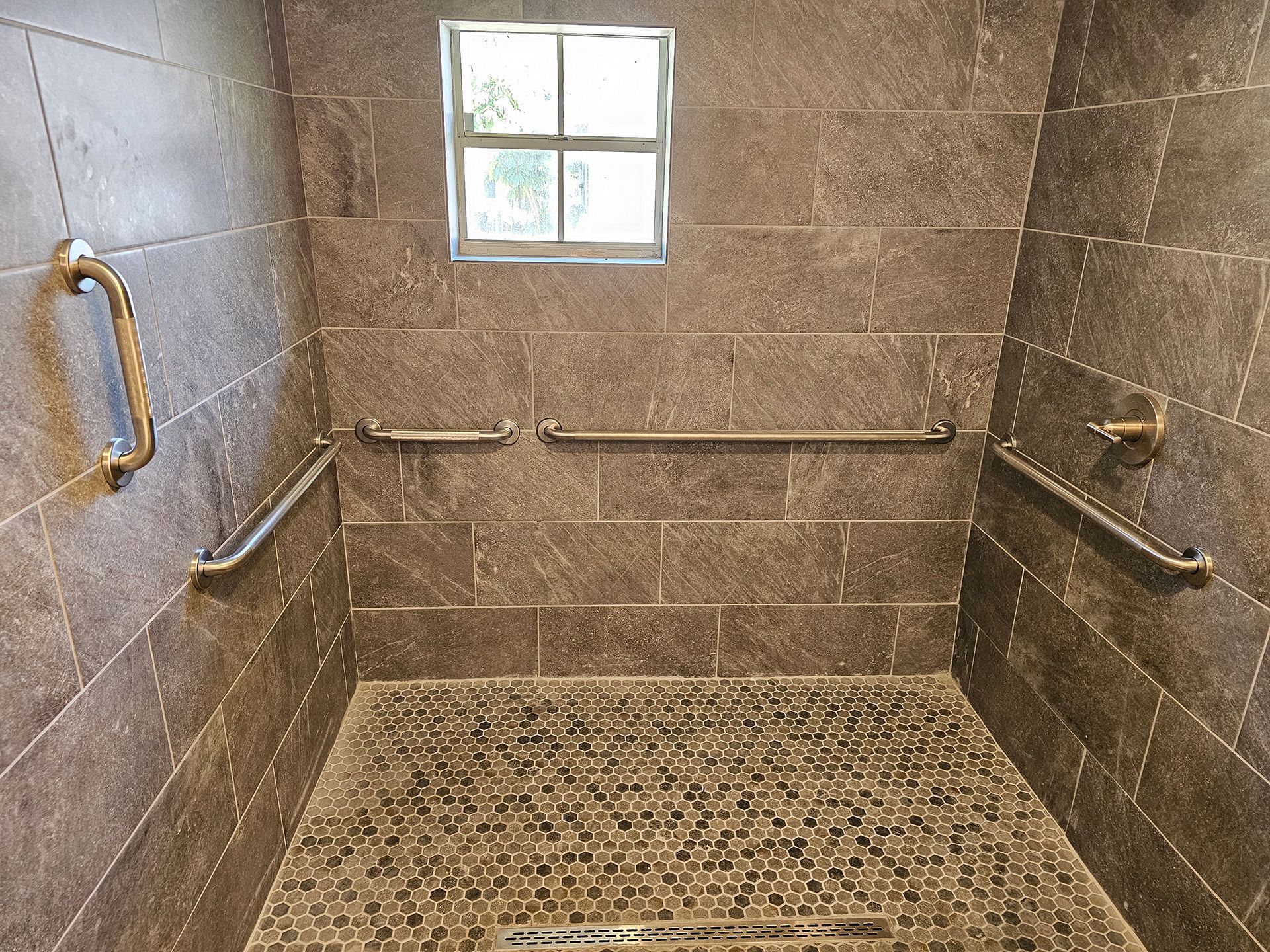A walk in shower with stainless steel handles and a window.