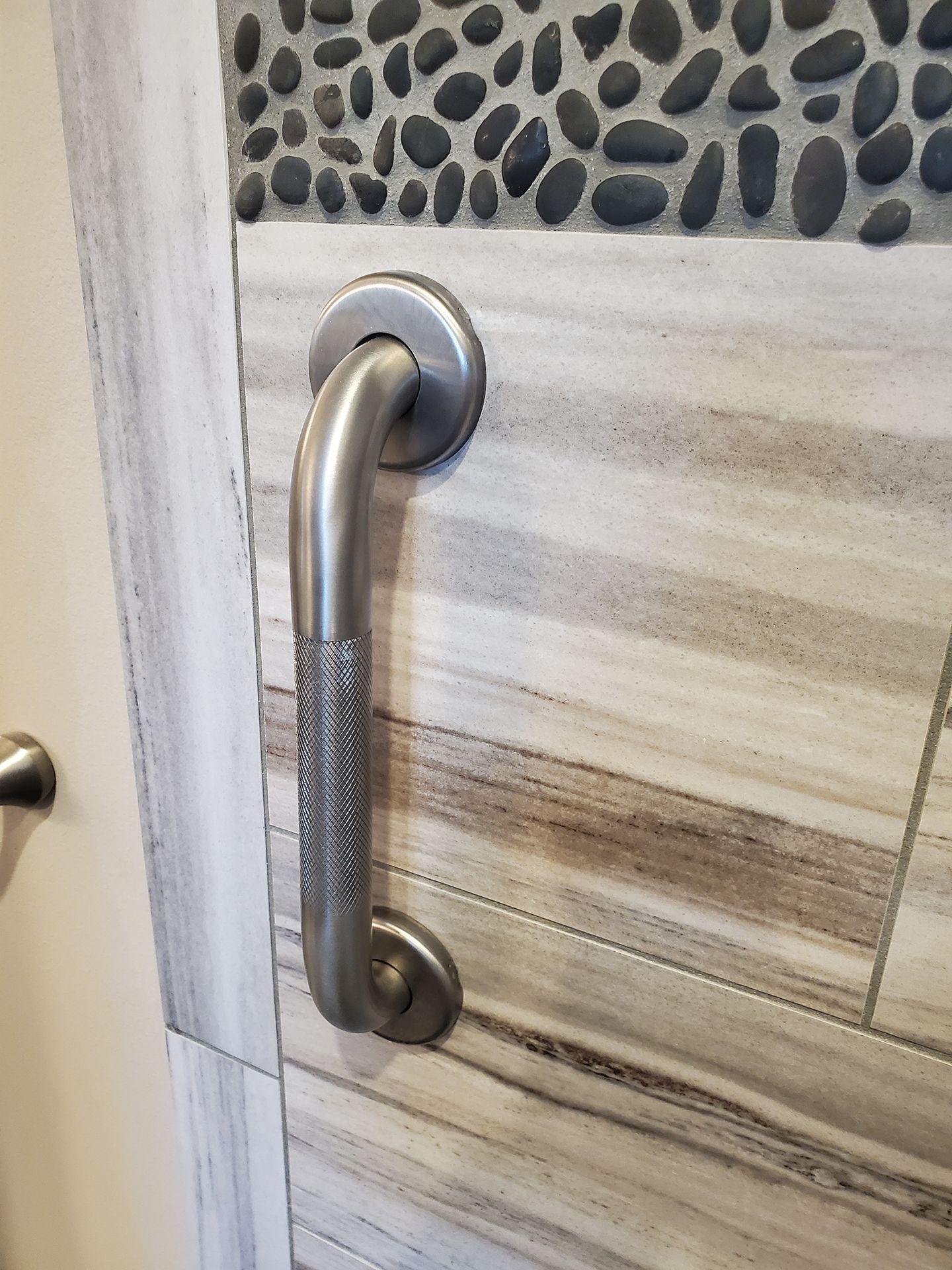A stainless steel handle is attached to a tiled wall.