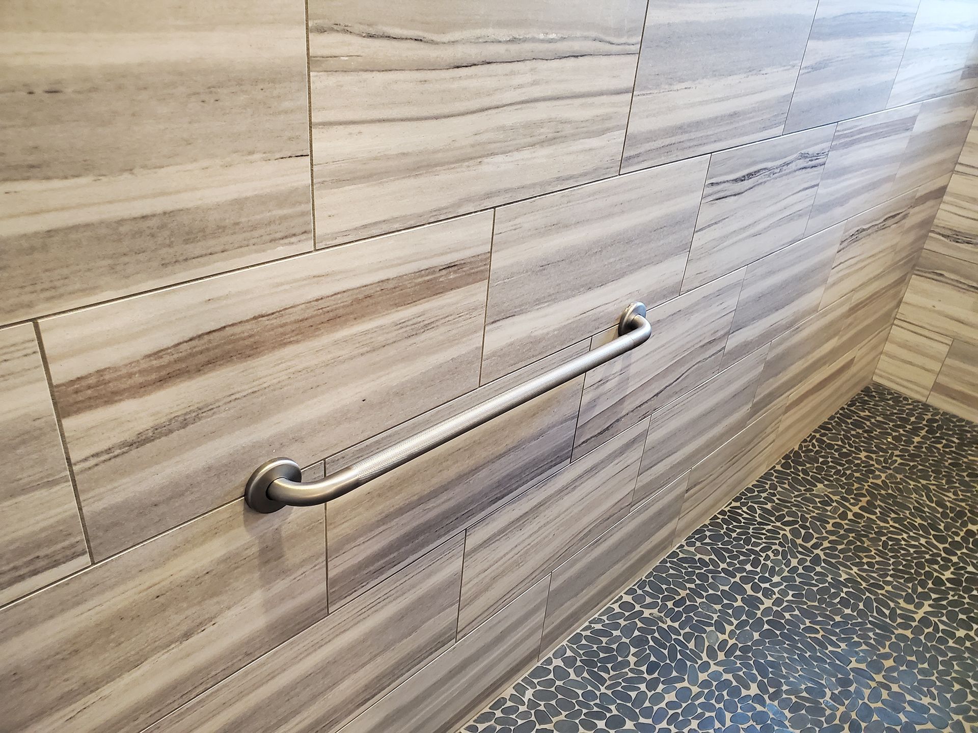 A stainless steel grab bar is attached to a tiled wall in a bathroom.
