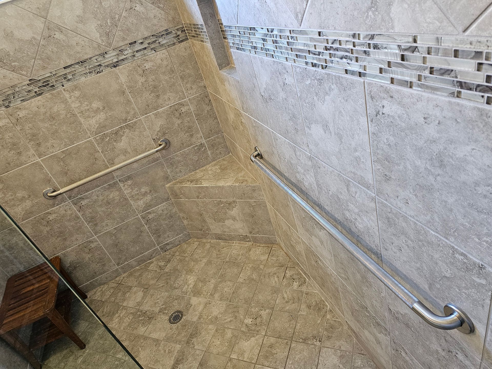 A bathroom with a walk in shower and a stainless steel hand rail.
