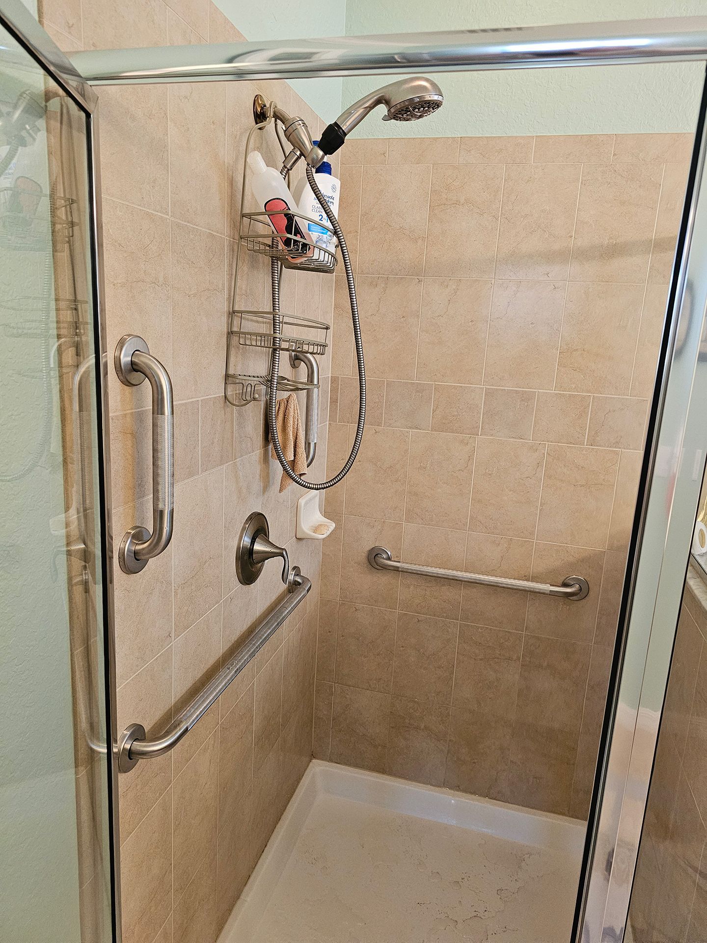 A shower with a shower head and a soap dispenser on the wall.