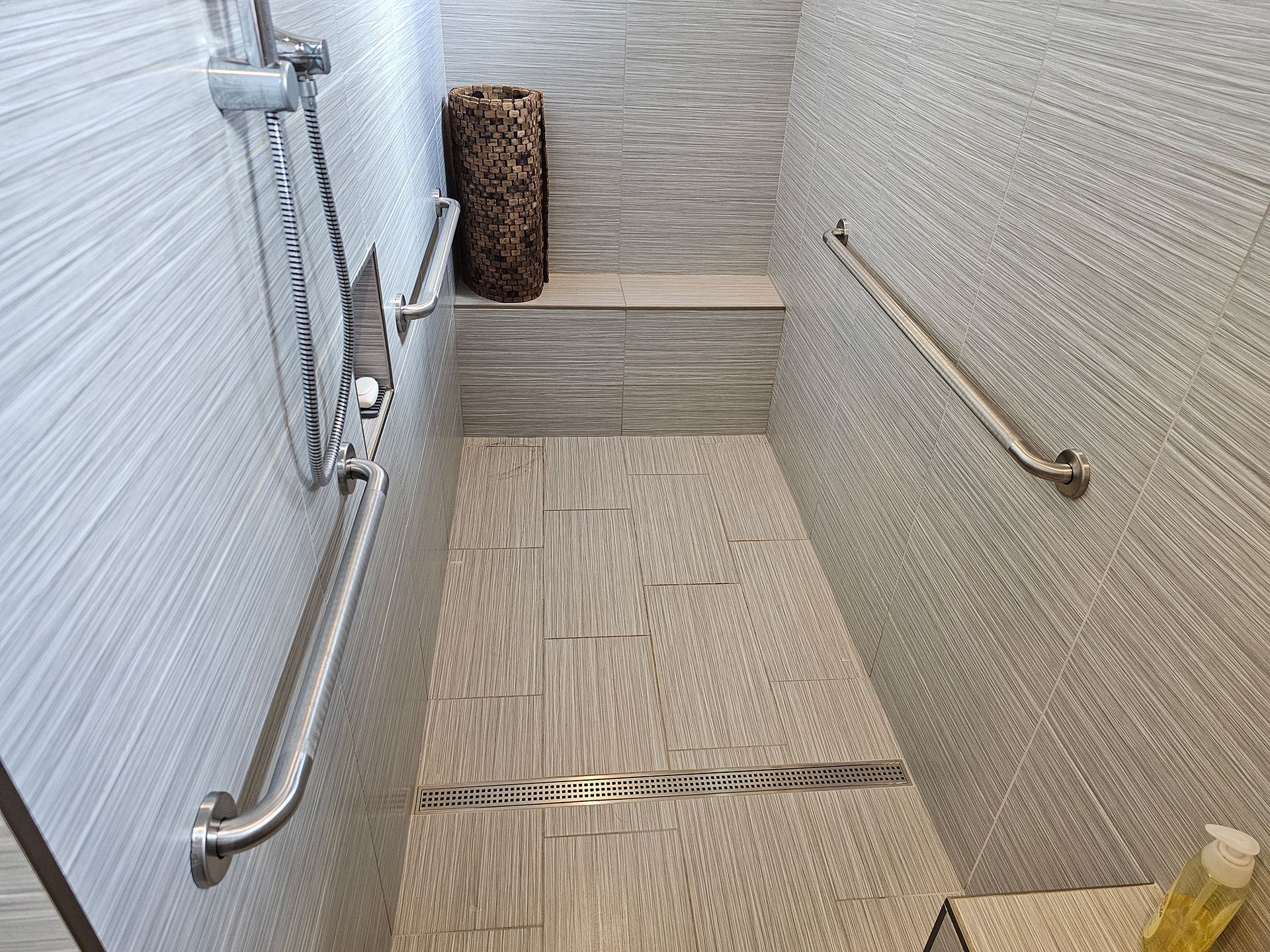 A bathroom with a walk in shower with stainless steel handles.