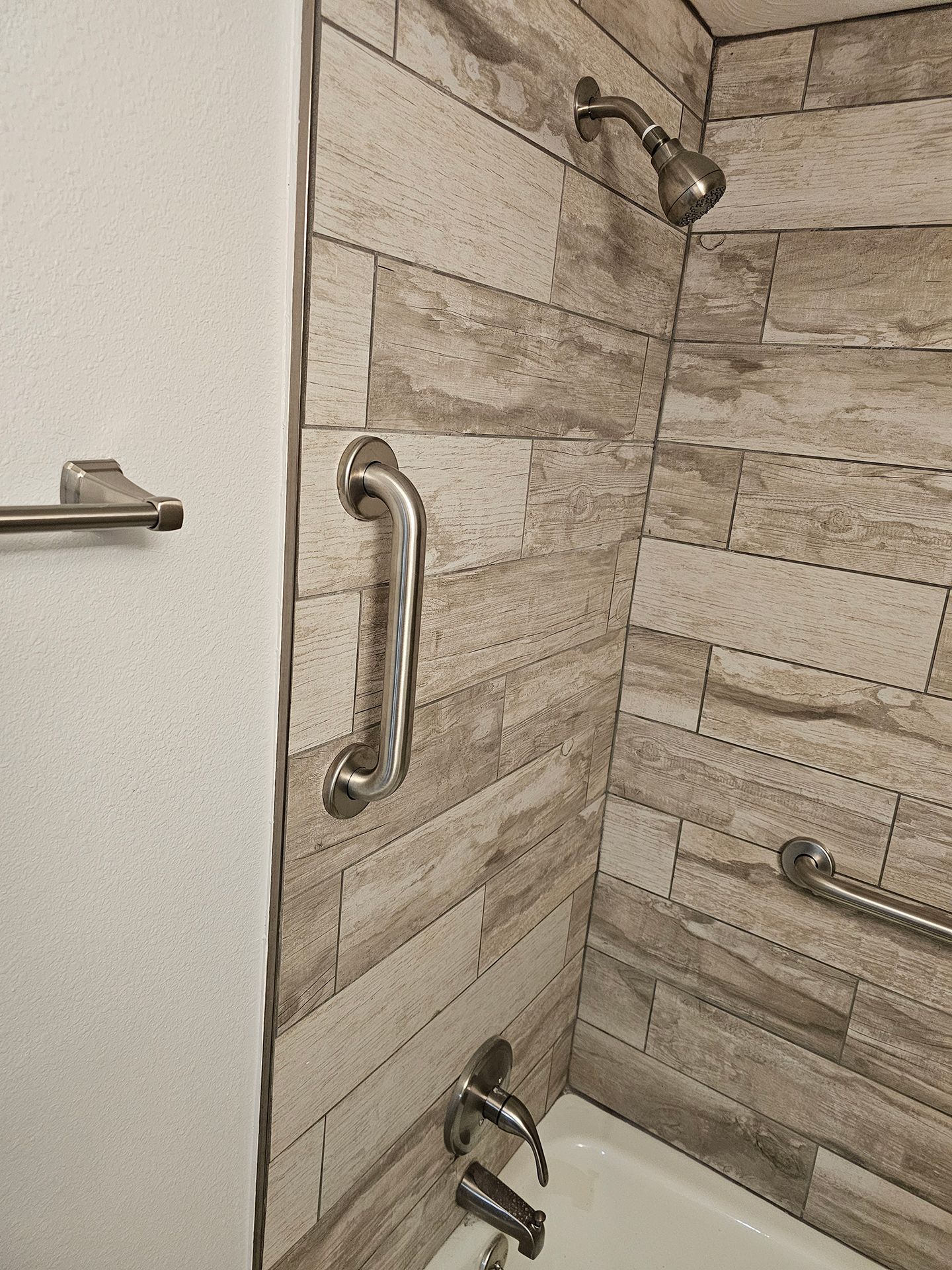 A bathroom with a bathtub, shower, and stainless steel handles.