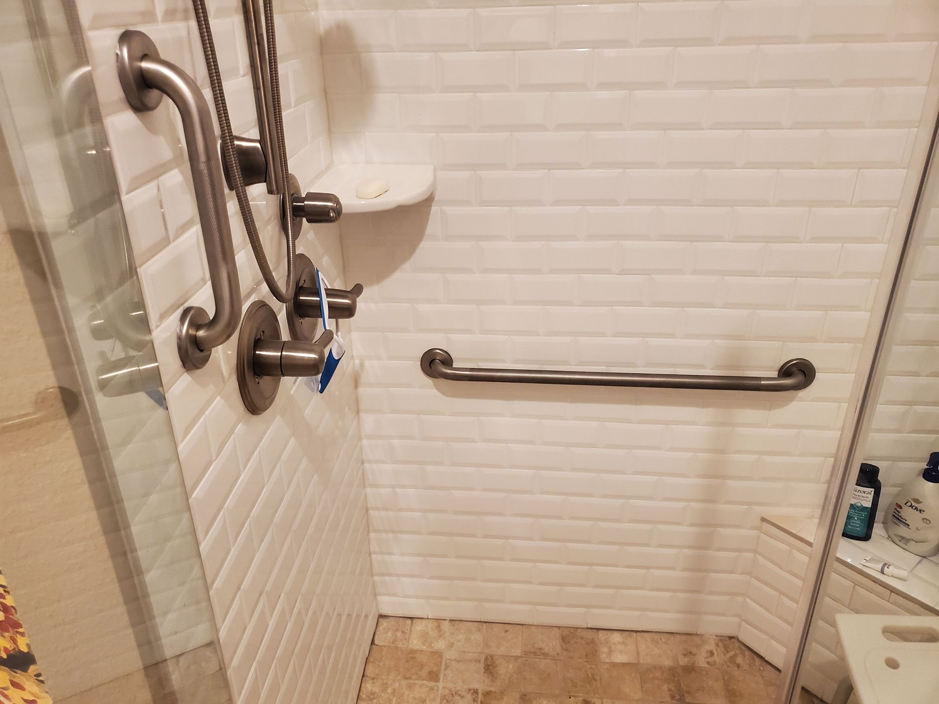 A bathroom with a walk in shower and stainless steel handles.