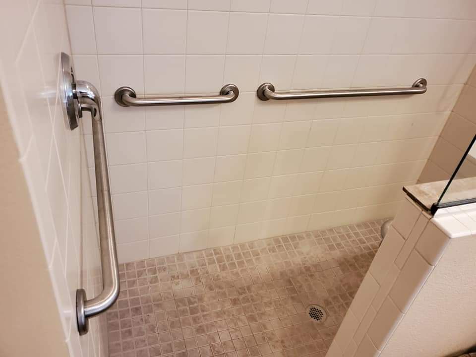A bathroom with a walk in shower and stainless steel handrails.