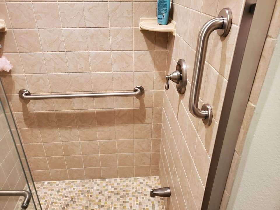 A bathroom with a walk in shower and stainless steel handles.