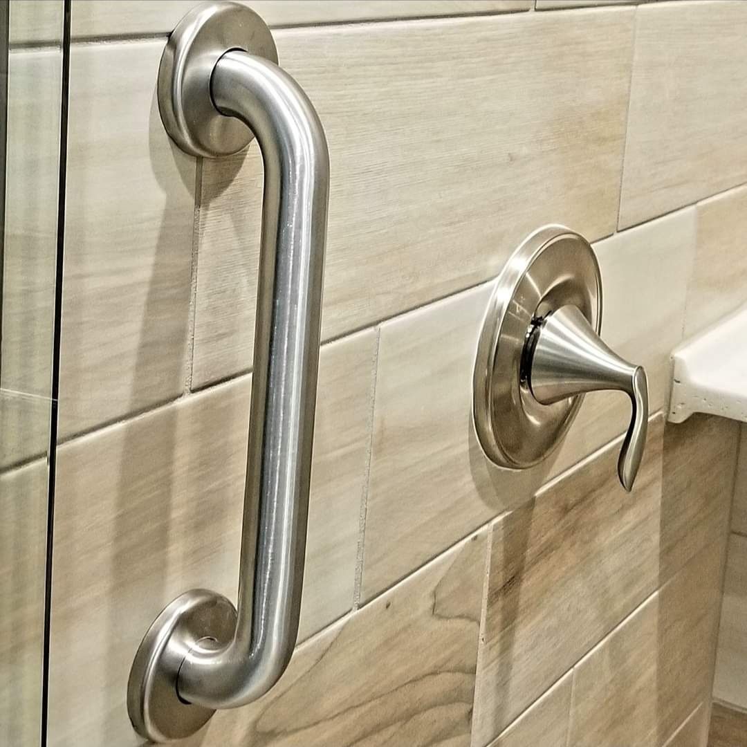 A stainless steel handle is attached to a tiled wall in a bathroom.