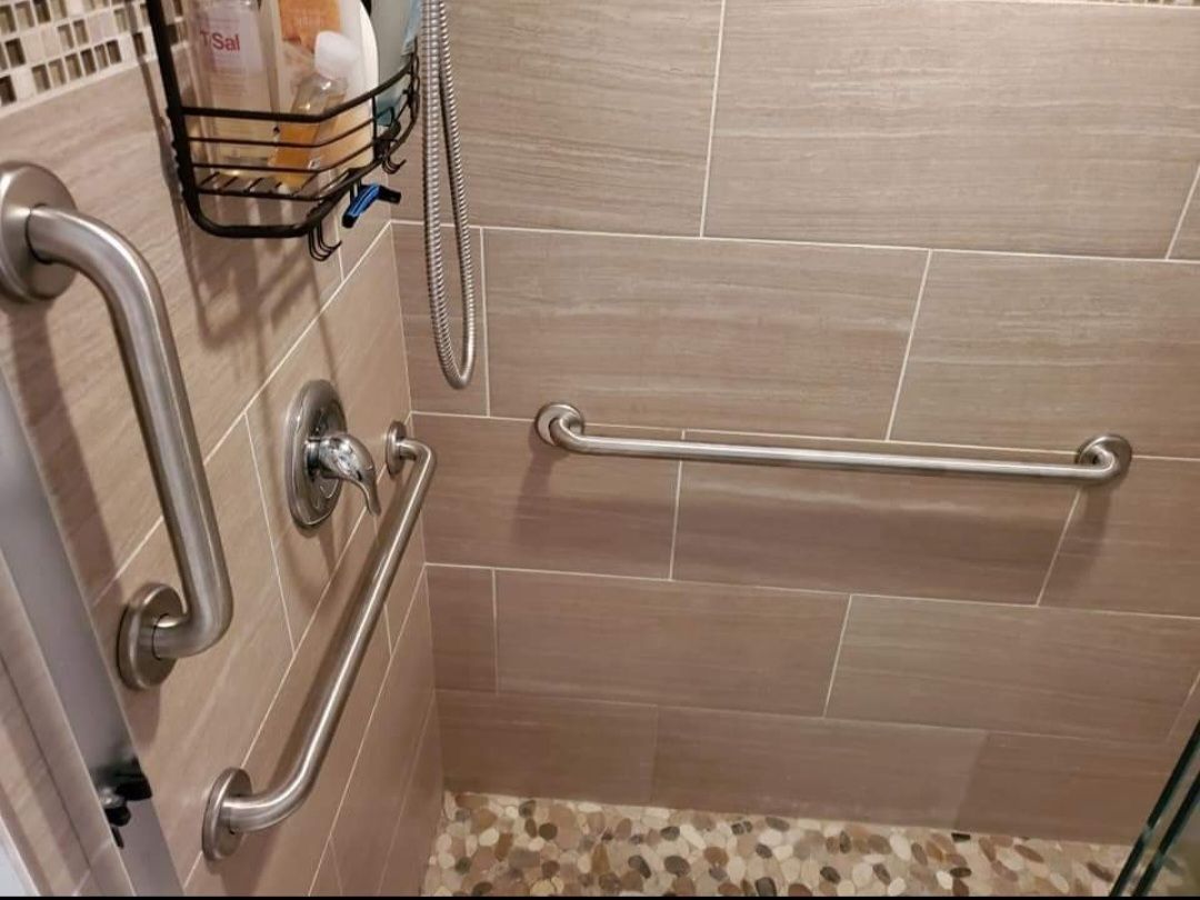 A bathroom with a walk in shower with stainless steel handles.