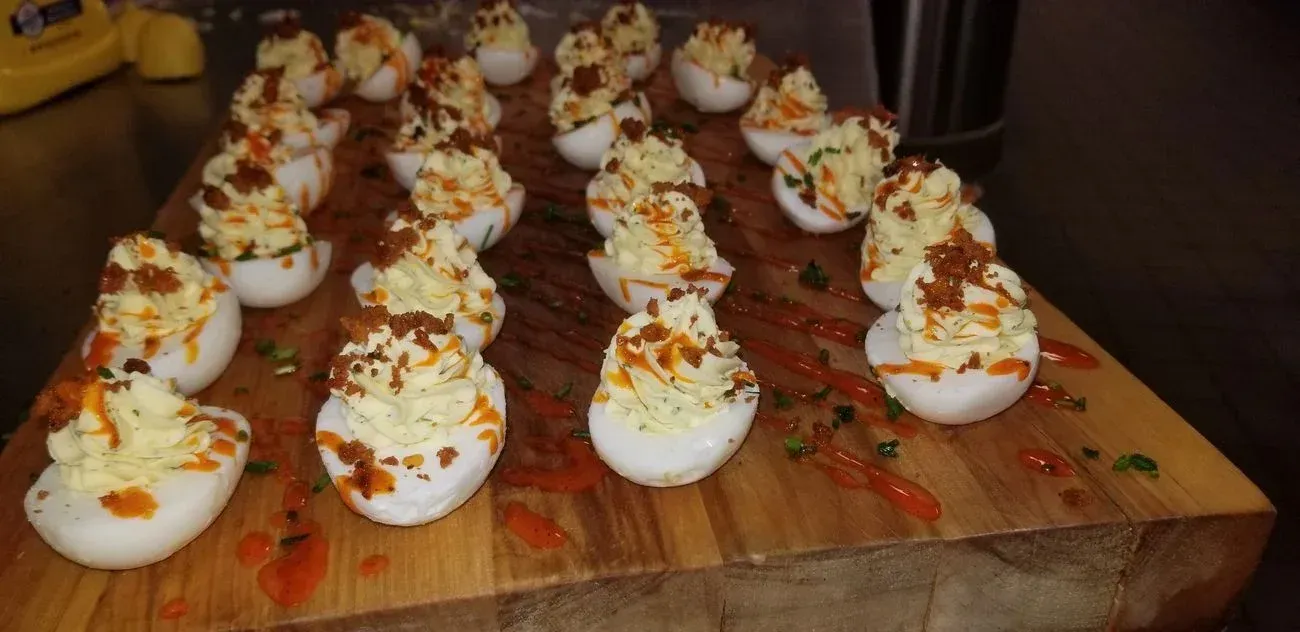 Deviled eggs topped with bacon on a wooden board.