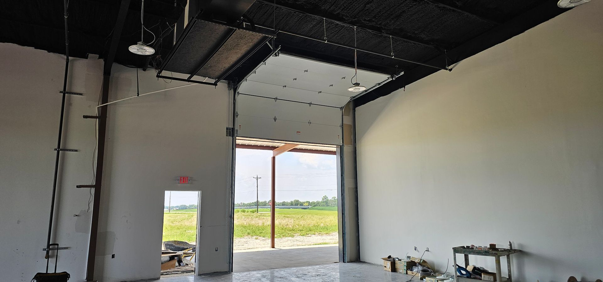 An empty building with a garage door open and a field in the background.