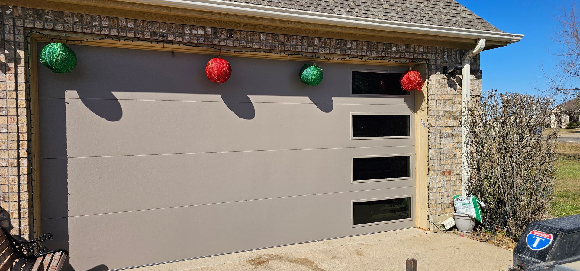 A garage door decorated for Christmas with red and green balls hanging from it.