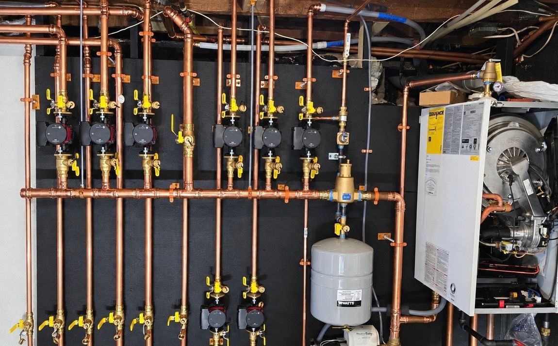 Commercial plumbing manifold with copper pipes, valves, pressure tank, and boiler in a mechanical room