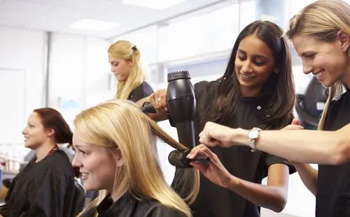 Hairdressers styling a client's hair in a salon. Blondes are working, smiling.