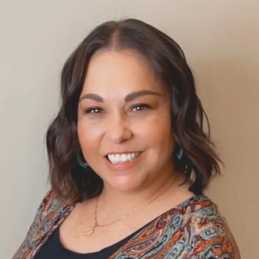 Bobbie Hotler with shoulder-length brown hair smiles, wearing a patterned top and necklace.