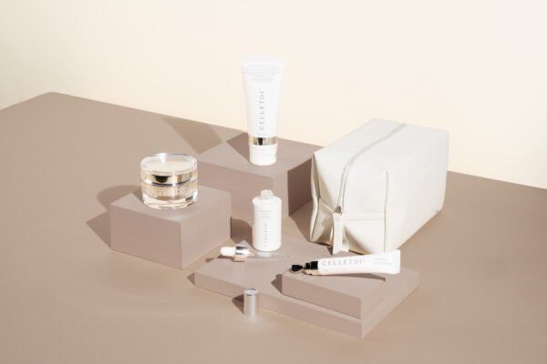 Skincare products arranged on blocks against beige background, including jars, tubes, and a cosmetic bag.