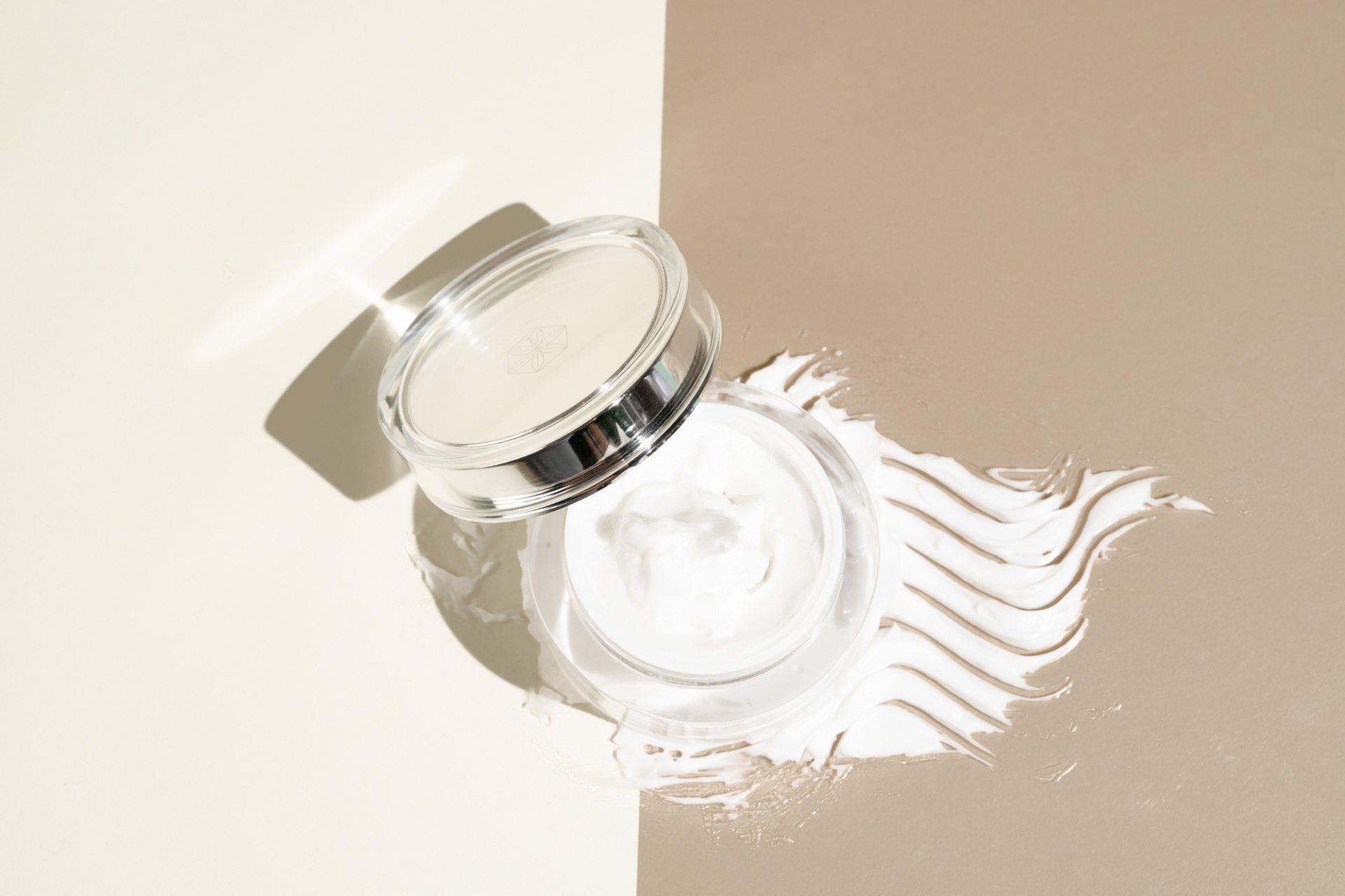Open jar of white powder on two-tone beige background, with a powder swatch and its shadow.