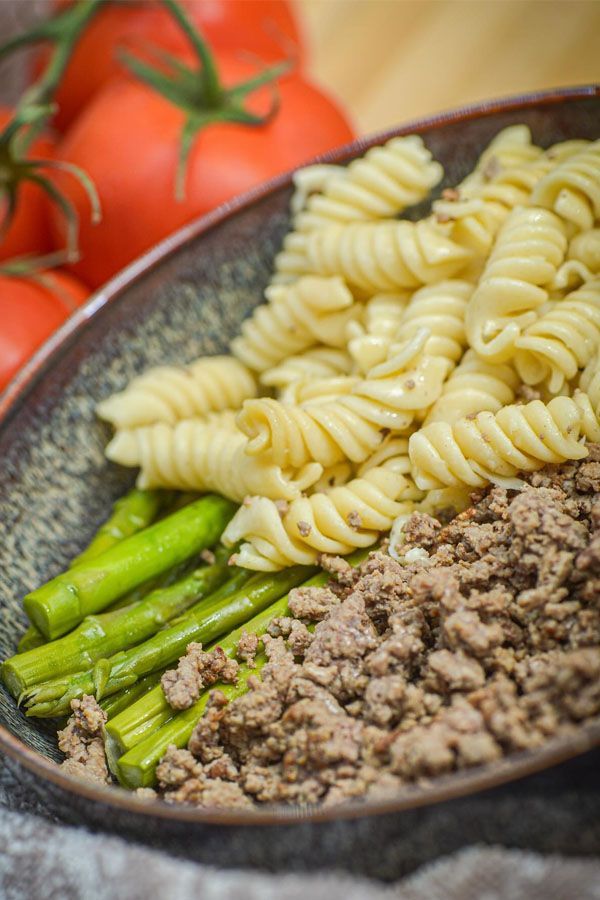 A close up of a plate of pasta , meat and asparagus.