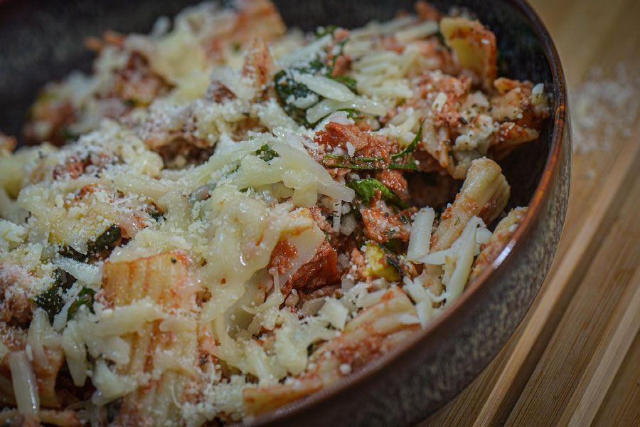 A bowl of pasta with tomato sauce and cheese on a wooden table.