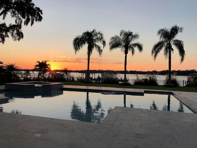Sunset over water with palm trees and a pool.
