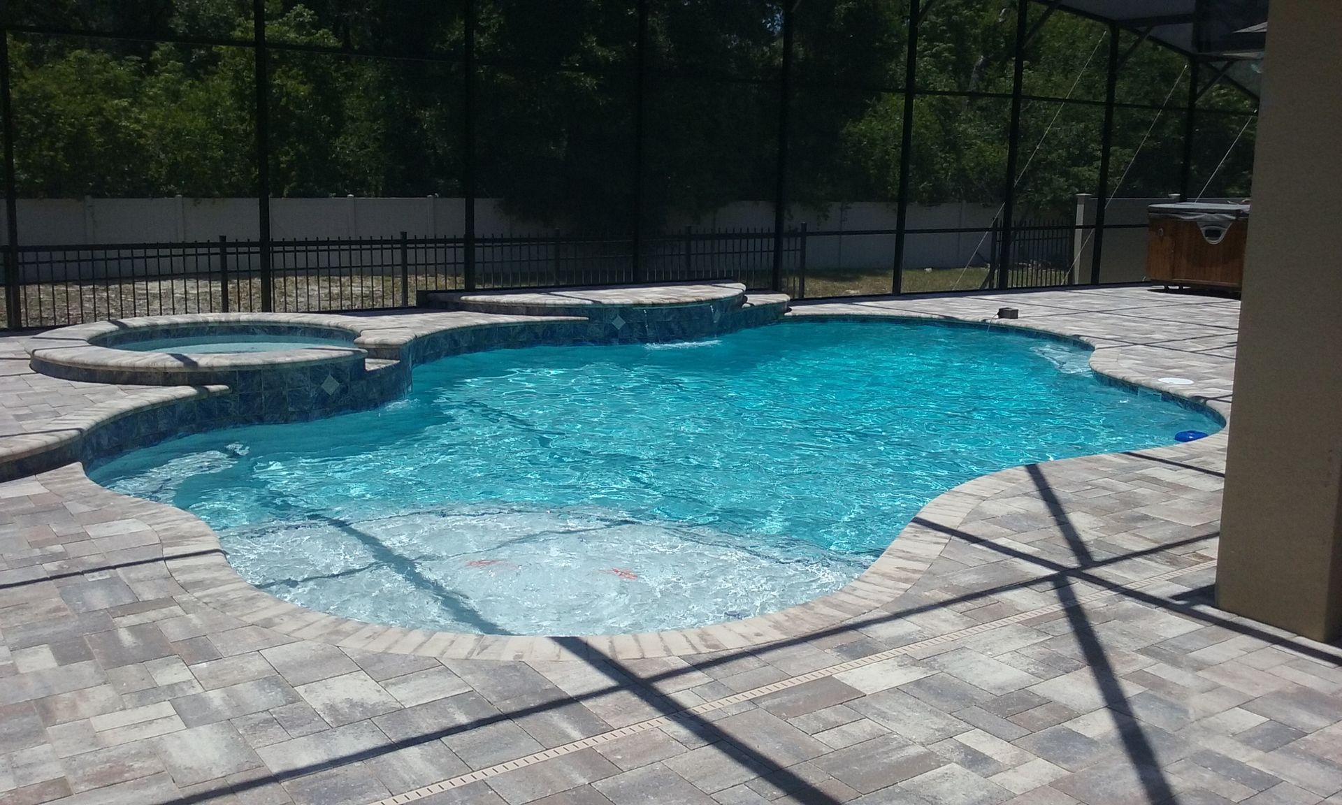 Swimming pool with adjacent hot tub and brick patio, enclosed by a black fence.