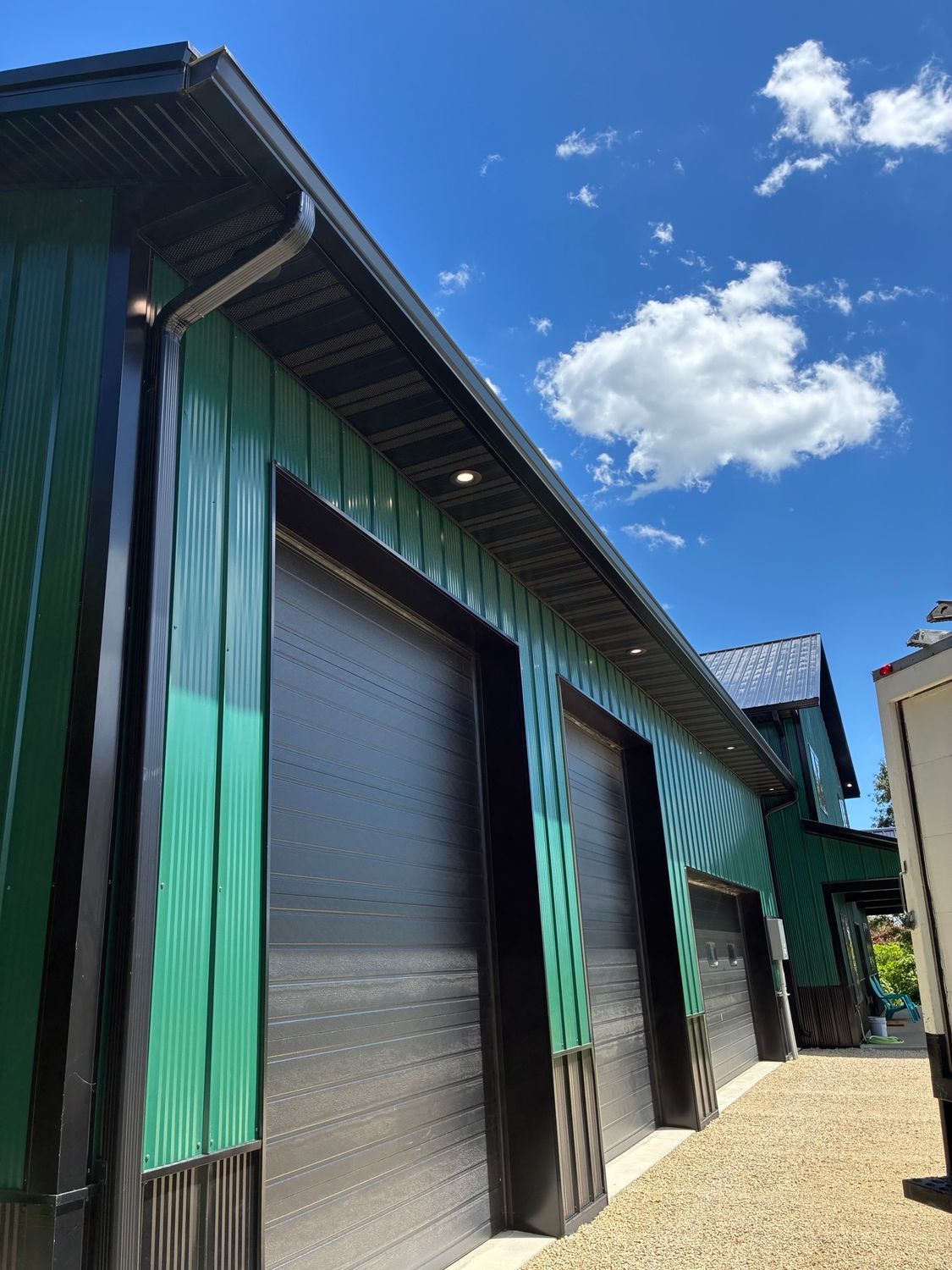 Row of turquoise garage doors under a blue sky with clouds, beside a gravel driveway